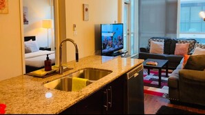 Une chambre d’hôtel moderne dotée d’un coin cuisine, d’un salon avec un canapé et une télévision, ainsi que d’une grande fenêtre offrant une vue dégagée.