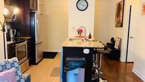 Une cuisine compacte équipée d’un réfrigérateur, d’un four et d’un évier. Il y a une horloge au mur et un petit îlot central avec un évier.