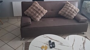 A modern living room with a sofa, two side tables, and a remote control on one of the tables. - Serene 1-bedroom Apartment in Bloemfontein (Bloemfontein)