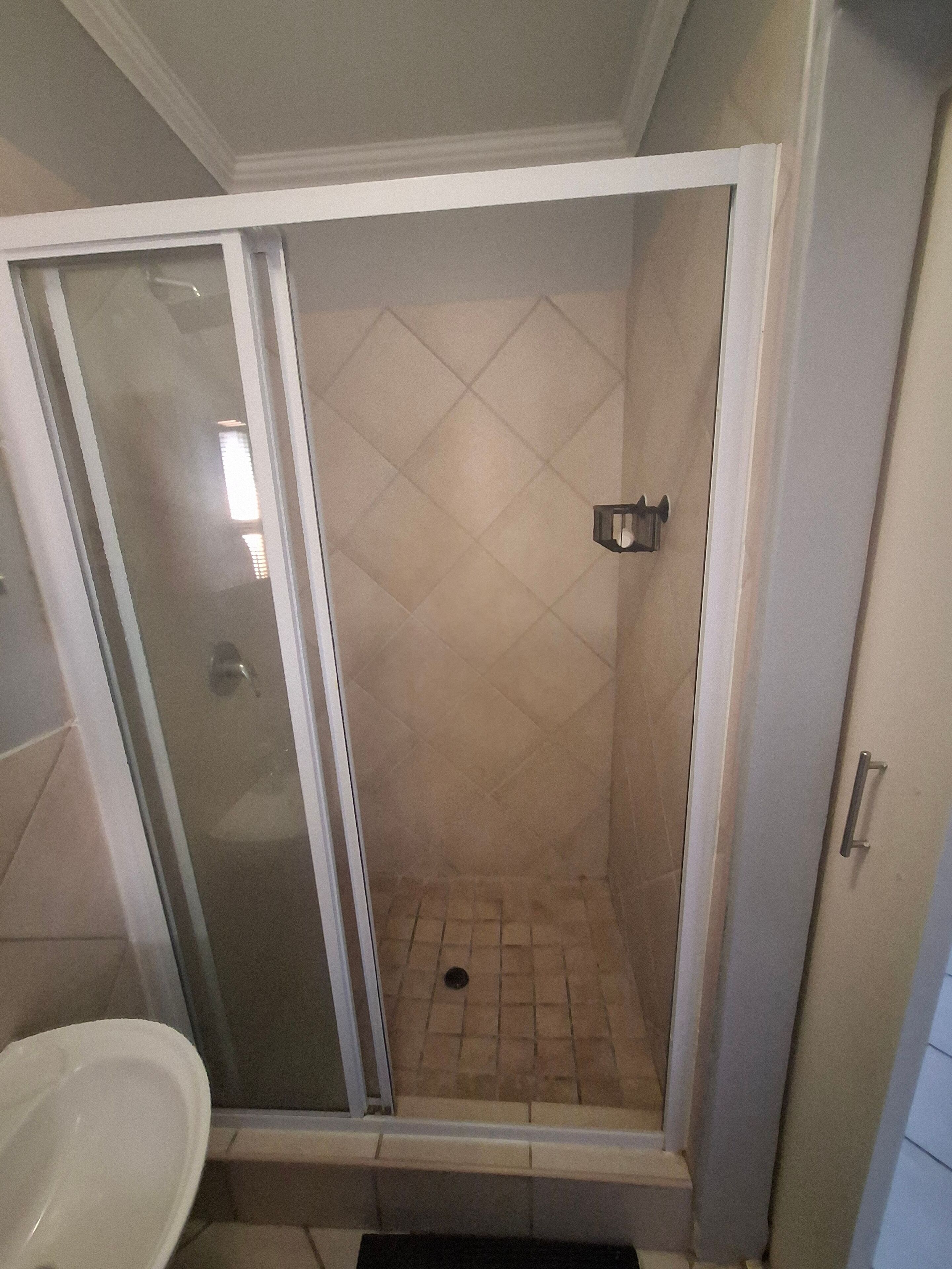 A shower with a glass door, a tiled floor, and a metal handle.
