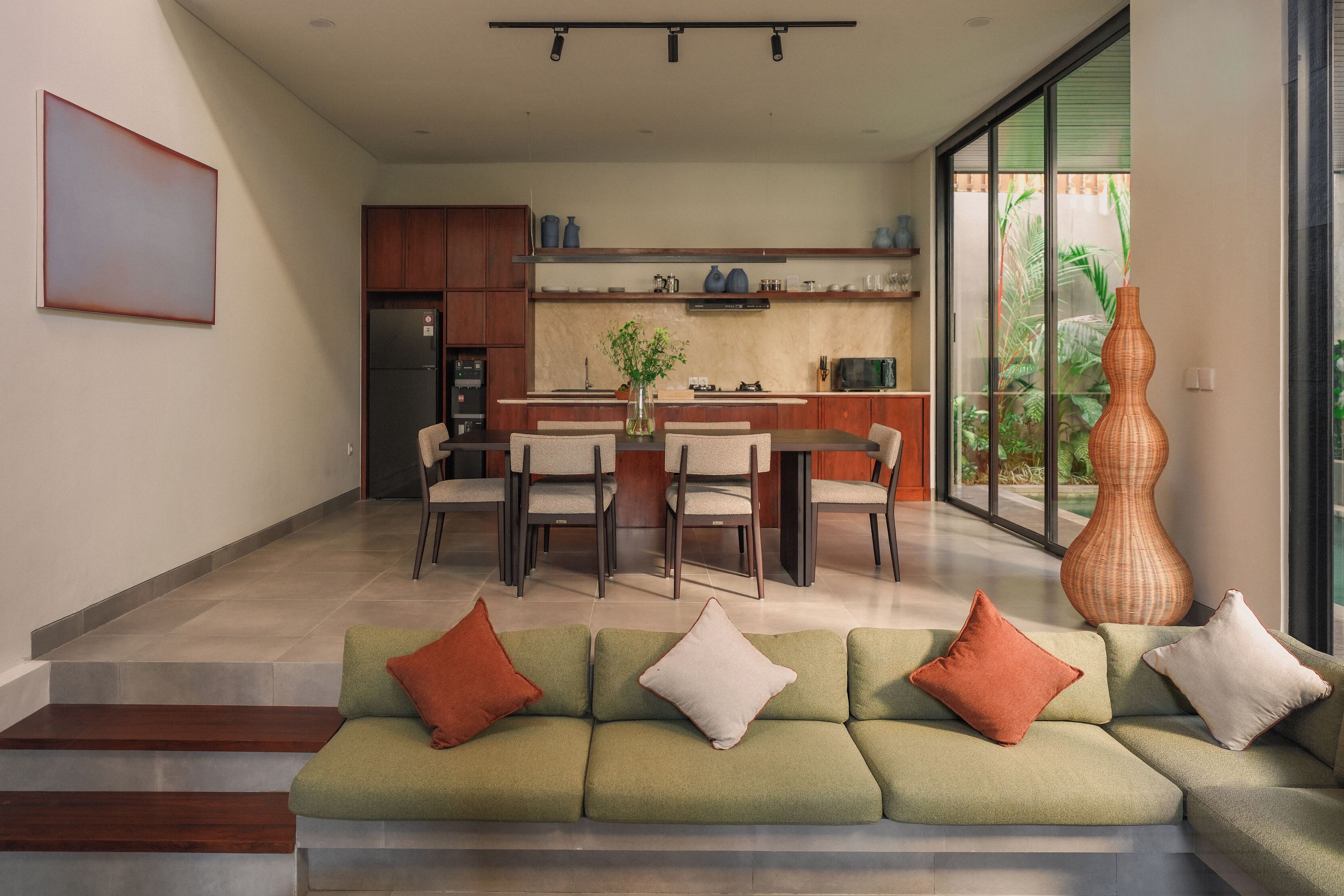 A modern kitchen with a dining area, a sofa with cushions, and a large vase.