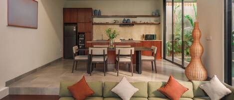 A modern kitchen with a dining area, a sofa with cushions, and a large vase.
