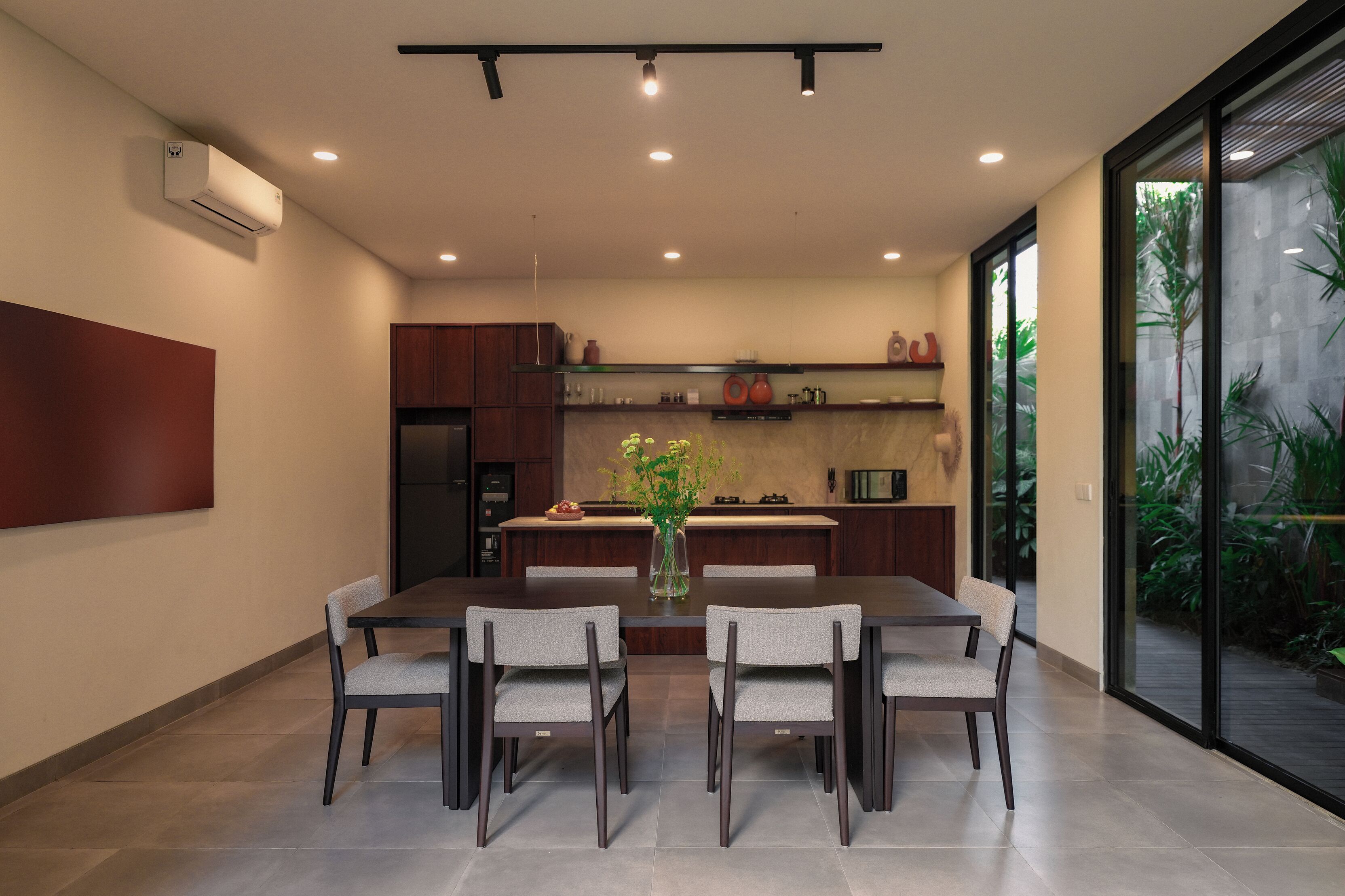 A modern kitchen with a central island, a dining area with a table and chairs, and a large sliding glass door leading to a garden.