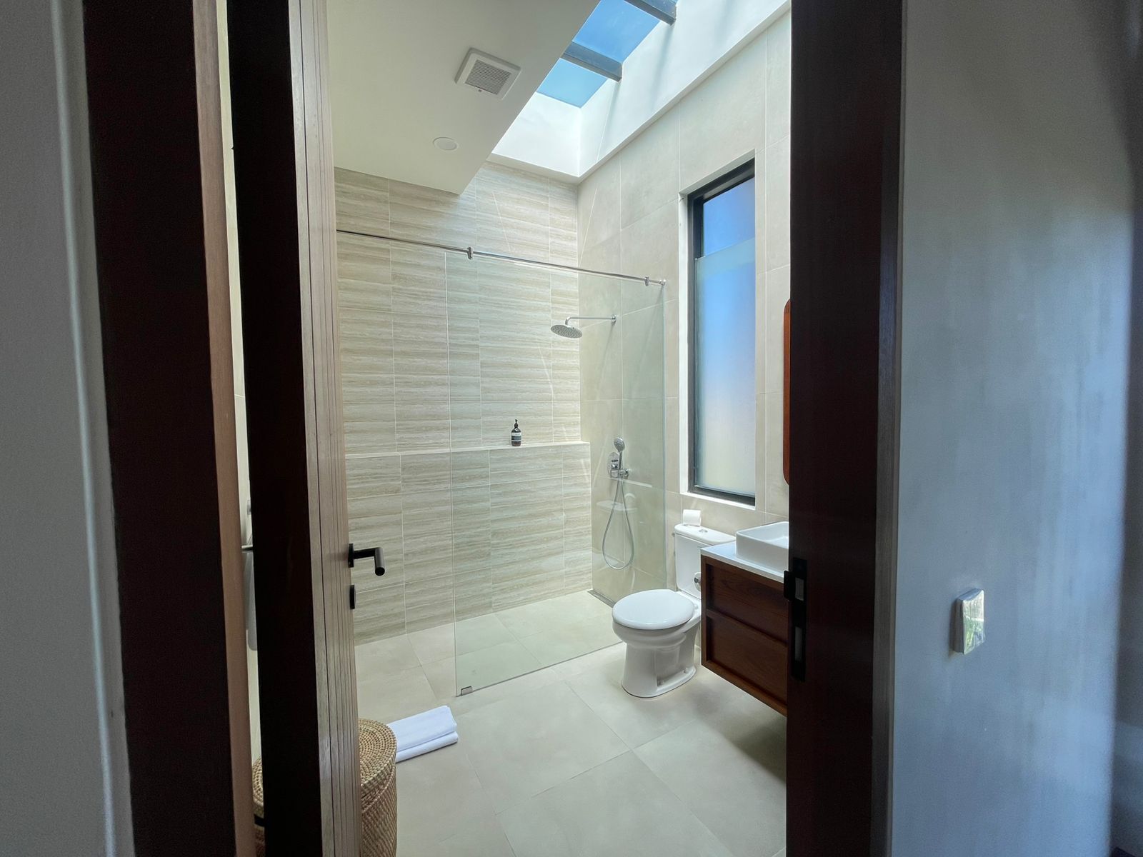 A modern bathroom with a skylight, a glass shower enclosure, and a white toilet.