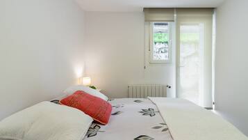 Ein Schlafzimmer mit einem Bett, einem Fenster, einer Heizung und einem Nachttisch mit einer Lampe.