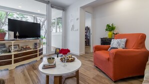 A modern living room with a flat-screen TV, a red sofa, a coffee table with books and a vase, and a bookshelf.