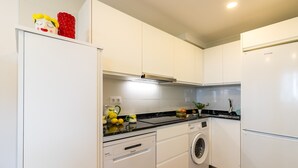 A compact kitchen with white cabinets, a washing machine, a dishwasher, and a refrigerator.