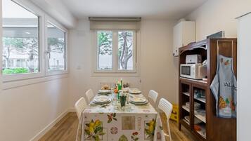 Et spiseområde med et bord dækket til fire personer, en mikrobølgeovn og et skab med køkkenudstyr.