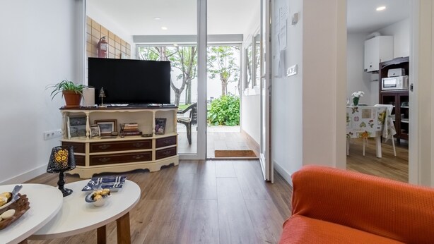 A living room with a flat-screen TV, a sofa, a dining area with a table and chairs, and a kitchen area with cabinets and appliances.