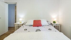 A bedroom with a bed, two bedside tables with lamps, a red pillow, and a small plant on one of the tables.
