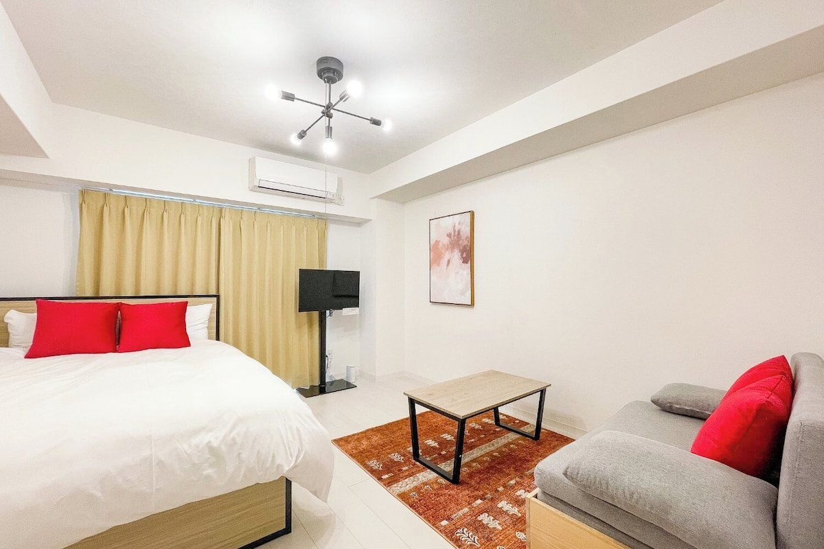 A hotel room with a bed, a sofa, a TV, an air conditioning unit, and a ceiling fan.