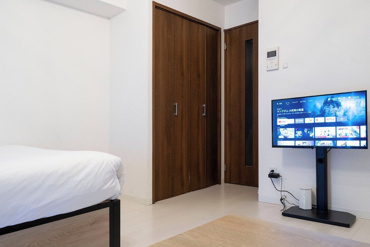 Une chambre à coucher comprenant un lit, un téléviseur, une armoire en bois et un thermostat fixé au mur.