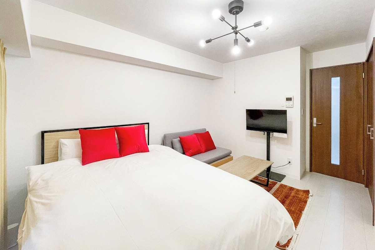 A bedroom with a bed, a TV, a desk, and a door.