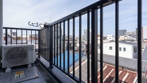 En balkon med udsigt over bybilledet, en Fujitsu airconditioner og gelænder af metal.