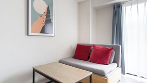 En moderne stue med en grå sofa, røde puder, et lille træbord og et indrammet abstrakt kunstværk på væggen.
