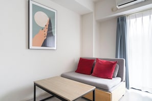 A modern living room with a grey sofa, red cushions, a small wooden table, and a framed abstract artwork on the wall. - Prandre DG (Osaka)