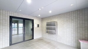 En lys, moderne lobby med flisegulv, en glasdør og et metalpanel til sikkerhed på væggen.