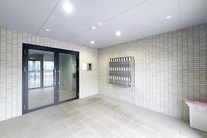 A clean, modern lobby with a tiled floor, a glass door entrance, and a metal security panel on the wall. - Prandre DG (Osaka)