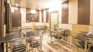 A room with multiple tables and chairs, wooden panel walls, and a ceiling with a grid pattern. - Hotel Pardesi's Near Mansa Devi Temple (Haridwar)