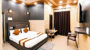 A modern hotel room with a large bed, a desk, two chairs, a TV, and a ceiling fan. - Hotel Pardesi's Near Mansa Devi Temple (Haridwar)