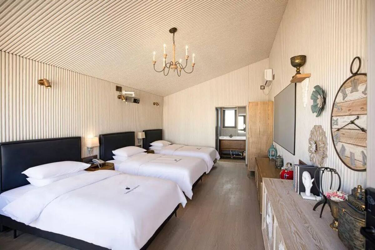 Une chambre d’hôtel avec trois lits, un lustre, une coiffeuse en bois et un miroir.
