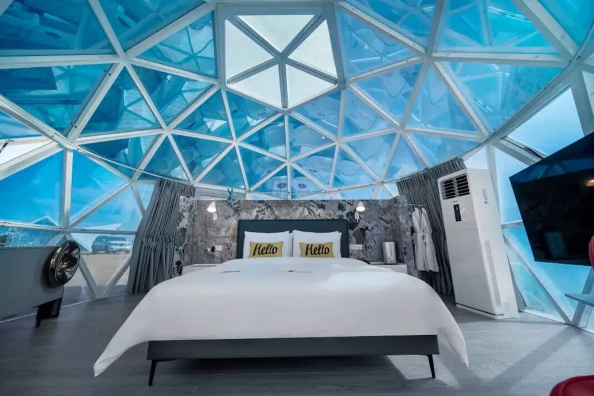 Une chambre moderne dotée d’un plafond en verre aux motifs géométriques, d’un grand lit et offrant une vue sur le ciel.