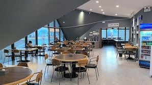 Una cafetería moderna con mesas y sillas redondas, una máquina expendedora y un cartel que da la bienvenida a todos.