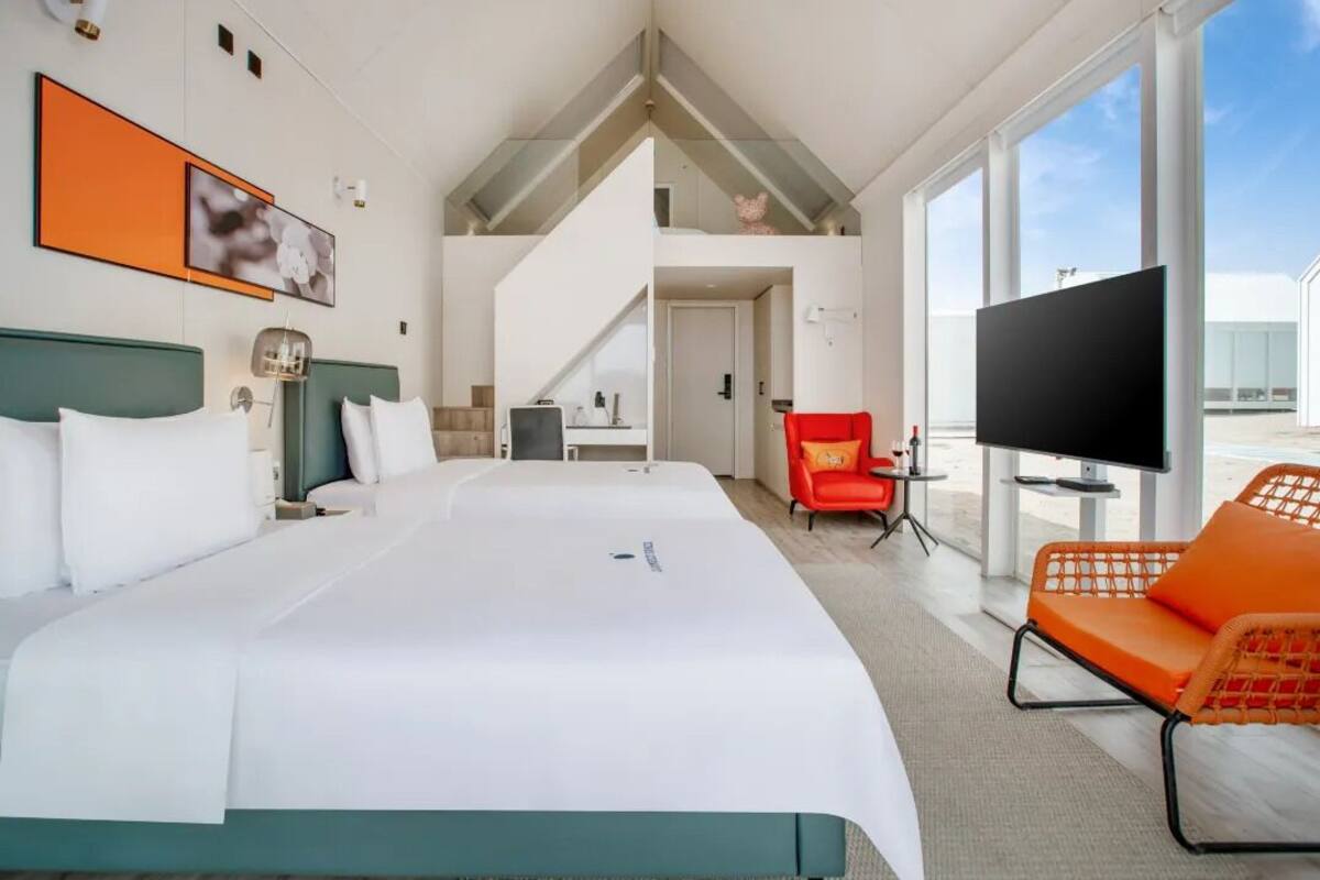 Une chambre d’hôtel avec un grand lit, une télévision, un fauteuil rouge et un escalier menant à un étage supérieur.