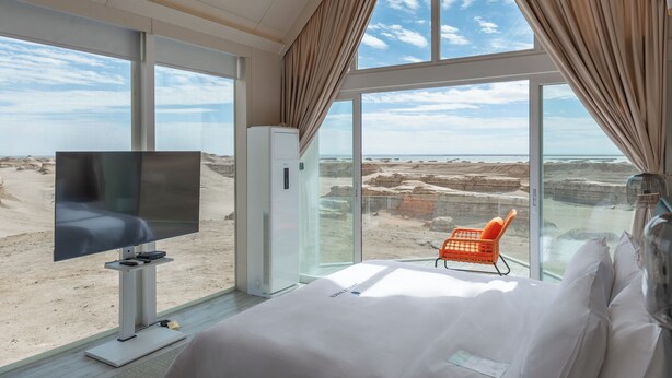 Un dormitorio con un ventanal grande, televisor, cama y una silla.