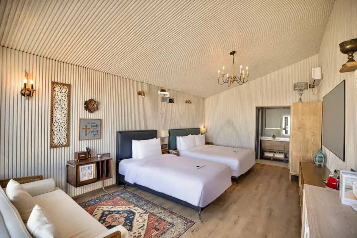 Une chambre d’hôtel avec deux lits, un canapé, un lustre, un miroir et une télévision.