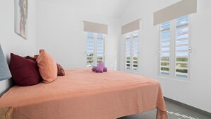 Ein Schlafzimmer mit Bett, Kissen, einem Gemälde und Fenstern mit Fensterläden.