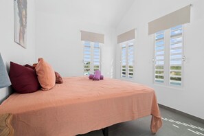 A bedroom with a bed, pillows, a painting, and windows with shutters. - Bon Bida di Watervillas #48b (Kralendijk)