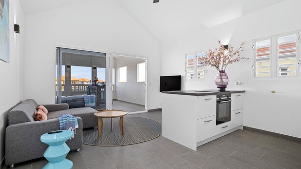 Eine moderne Wohnung mit Wohnbereich, Küchenzeile und einem Balkon mit Blick auf die Stadt.