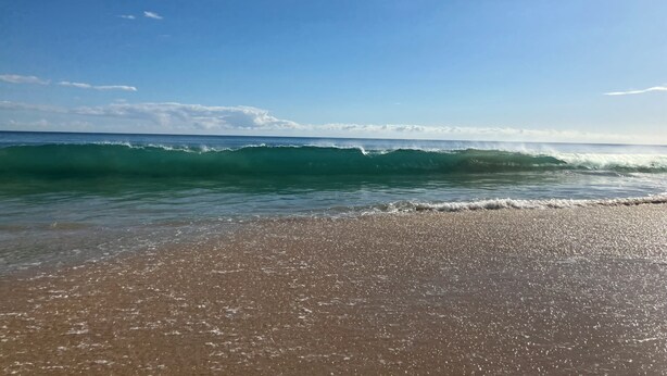 Una playa con olas, cielo despejado y un horizonte lejano.