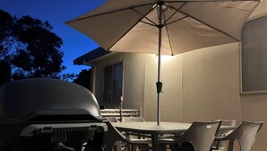 Un patio al aire libre con una mesa redonda y sillas, una parrilla y un paraguas grande.