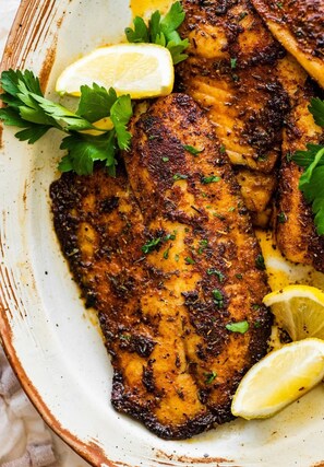 A dish of seasoned fish garnished with parsley and lemon slices. - Saint jean prestige hotel  (Kigali)