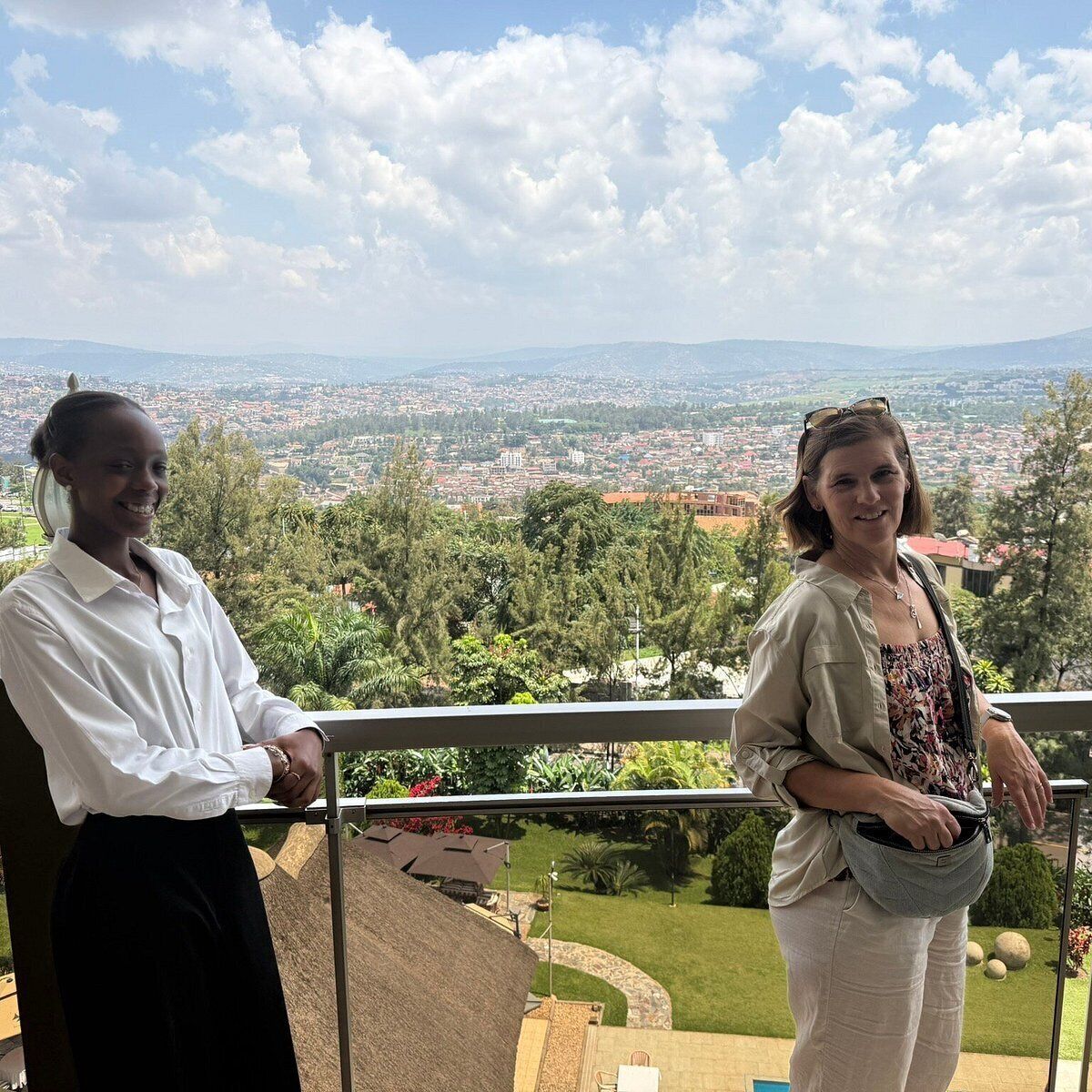 Deux personnes se tiennent sur un balcon, avec une vue sur le paysage urbain.
