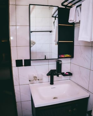 A bathroom with a white sink, black faucet, and a mirror above it. There is a towel rack with a white towel hanging on it. - Saint jean prestige hotel  (Kigali)