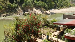 A riverside view with a garden area featuring potted plants and a red-roofed structure. - Chandresh Homestay (Aut)