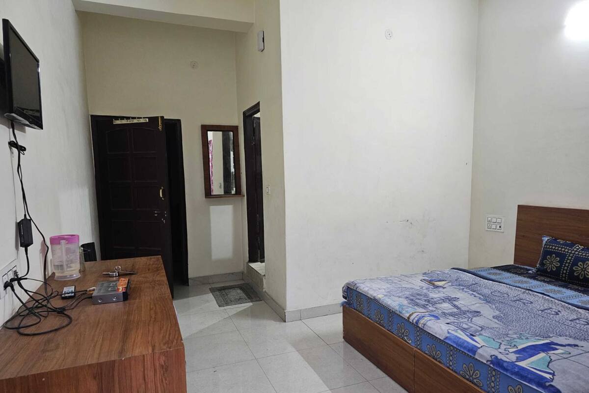 A bedroom with a bed, a desk, a TV, and a door leading to another room.