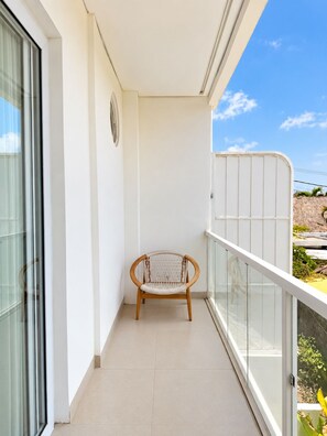Ein Balkon mit Korbstuhl, Glastür und weißer Brüstung.