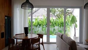 Una sala de estar moderna con comedor, grandes puertas correderas de vidrio y vistas a una piscina y plantas tropicales.