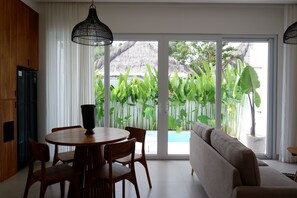 Un salon moderne comprenant un coin repas, de grandes portes-fenêtres coulissantes et une vue sur une piscine et des plantes tropicales.