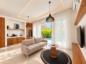 A modern living room with a sofa, a round wooden coffee table, and a TV mounted on the wall. - The Cosmos Villa - Balangan Pecatu Bali (Ungasan)