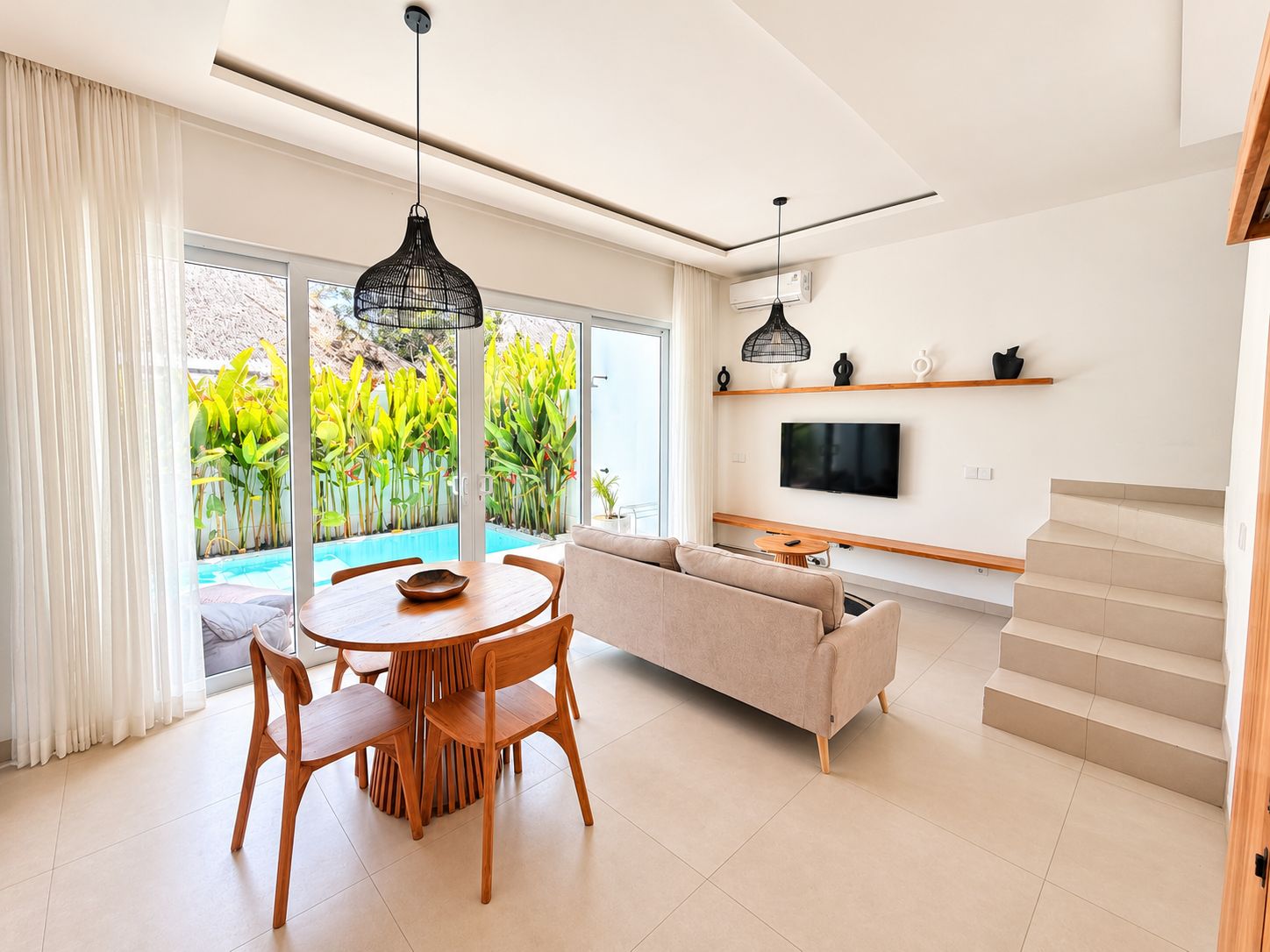A modern living room with a sofa, dining table, chairs, and a TV mounted on the wall.