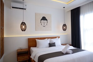 Une chambre d’hôtel avec une tête de lit en bois, du linge de lit blanc, une œuvre d’art représentant un Bouddha, deux lampes suspendues et une table de chevet avec un panier.