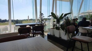 A restaurant with large windows, tables, chairs, and potted plants. - Relax & Play Panoramic Golf Vinaroz (Sant Jordi)