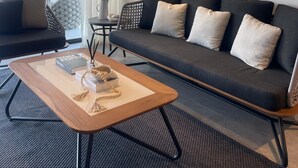 Un salon moderne avec un canapé foncé, une table basse en bois et une vue sur des palmiers à travers de grandes fenêtres.