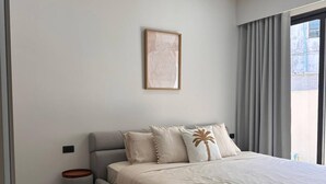 Une chambre moderne avec un grand lit, un ventilateur de plafond, une œuvre d’art encadrée et une fenêtre avec des rideaux.