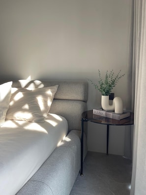 A neatly made bed with pillows, a small side table with a plant and books, and a curtain partially drawn. - Two-bedroom Suite with Seaview in Choengmon Beach (Chang Wat Surat Thani)